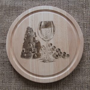 A round wood cutting board with a laser engraved design of cheese, wine and grapes